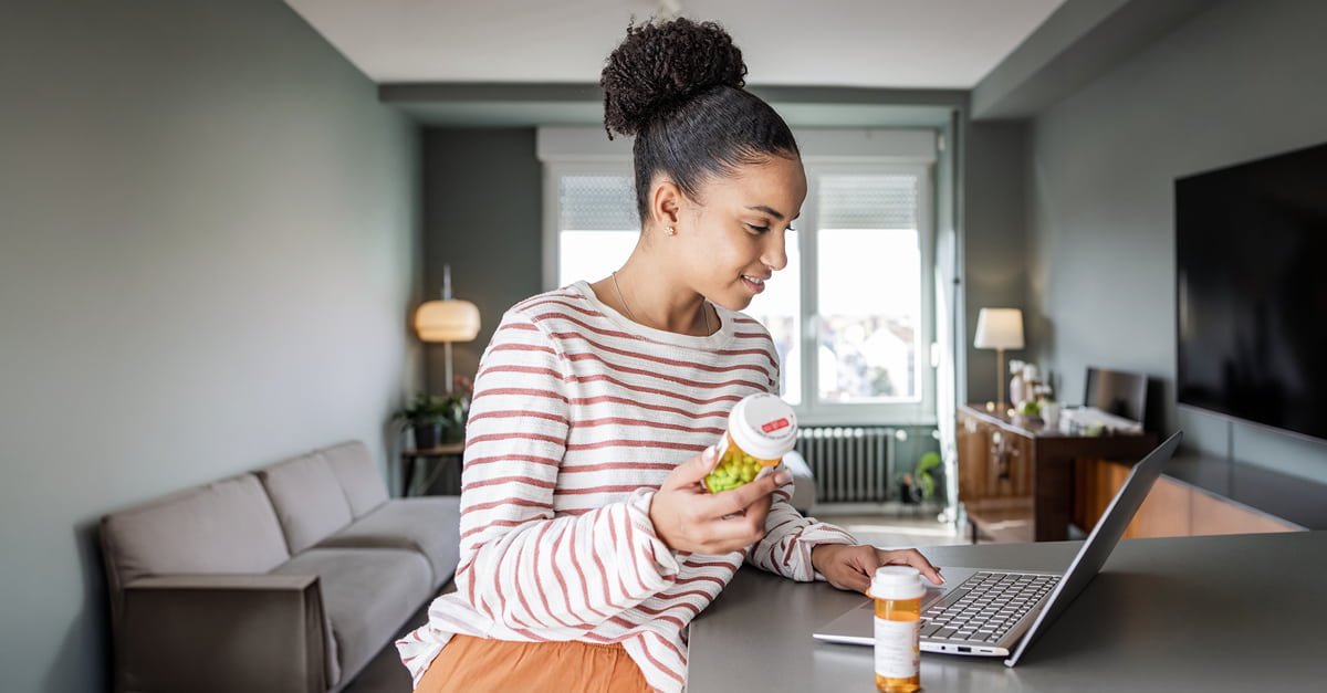 Woman holding a prescription bottle, looking up information on a laptop.