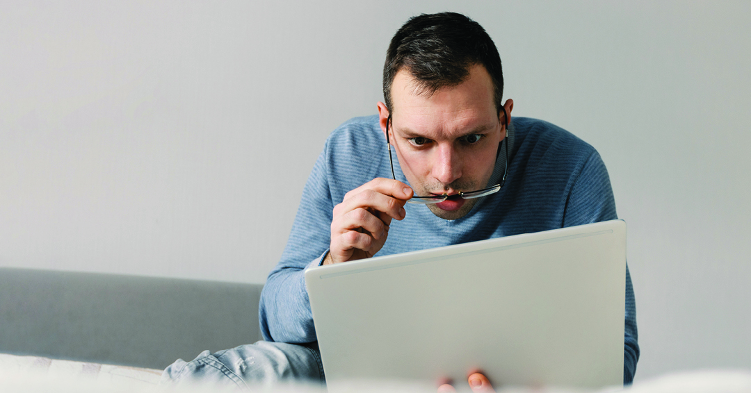 A man displaying a shocked expression gazes at the screen of tablet.